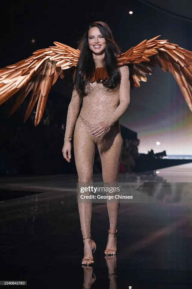 Adriana Lima walking a runway in a winged outfit and heels.