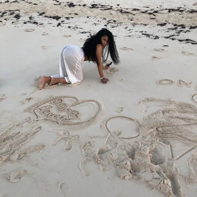 Nicki Minaj crawling barefoot on a sandy beach.
