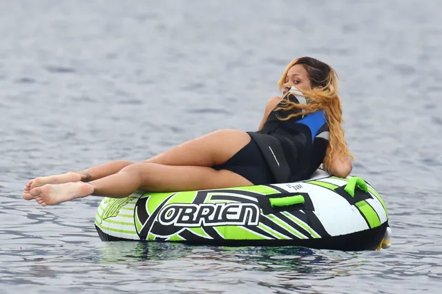 Rihanna floating on an inflatable ring with bare legs stretched out.