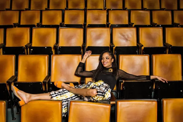 Tessa Thompson reclining across cinema seats in a fashion portrait.