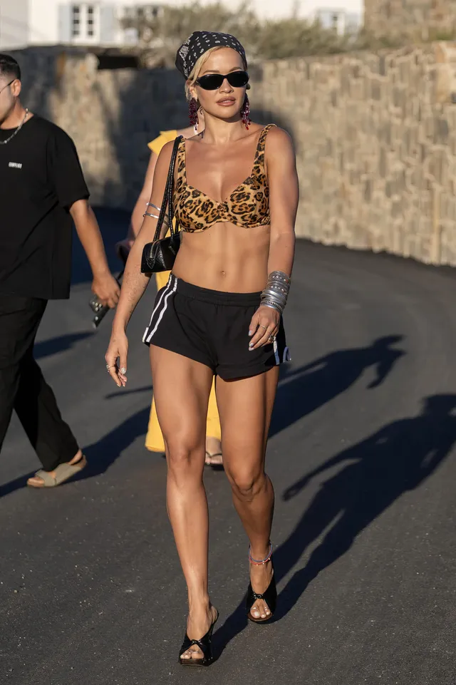 Rita Ora walking outdoors in shorts and black heels.