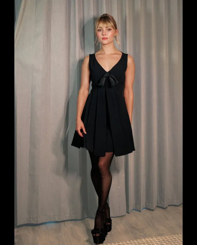 AnnaSophia Robb posing indoors in a black dress and platform heels.