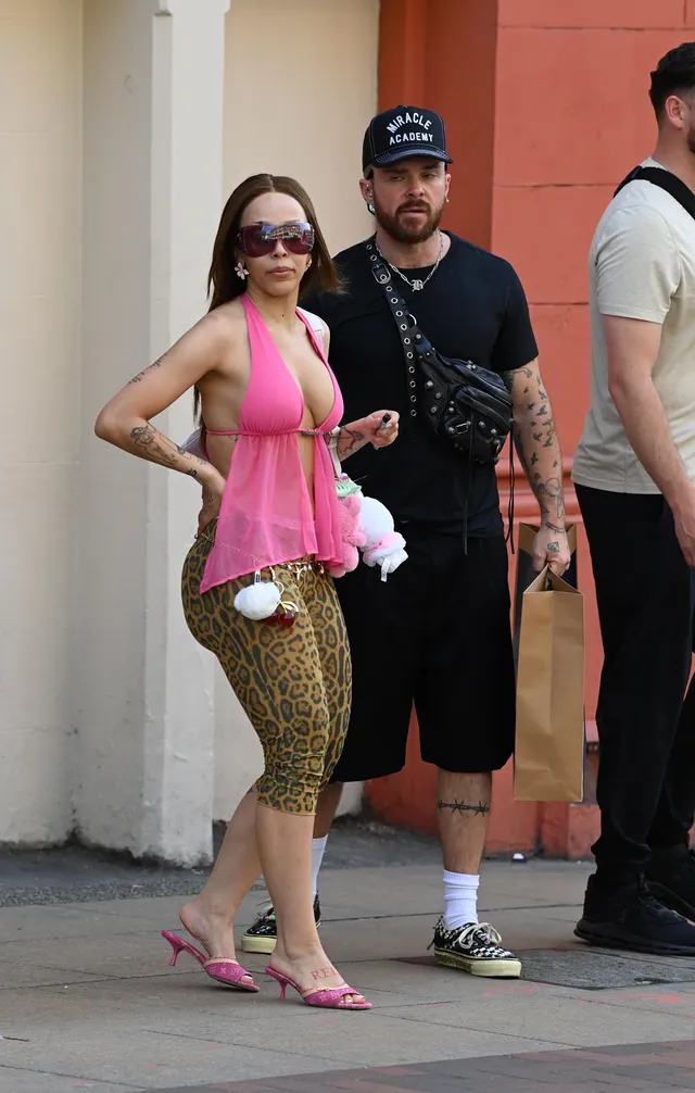 Doja Cat standing outdoors in a pink top, patterned shorts and pink heels.