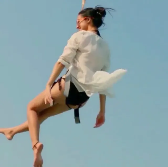 Disha Patani jumping barefoot in a pale shirt and dark shorts.