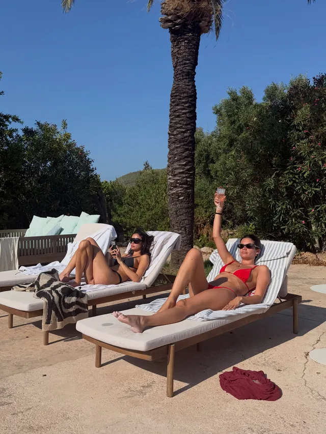 Sara Sampaio relaxing barefoot on a pool lounger beside a companion.