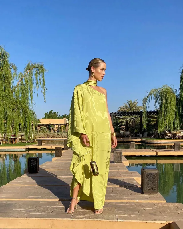 Claire Holt walking beside a pool in a yellow outfit.