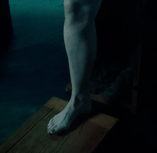 Monica Bellucci a dimly lit screen detail of a bare foot on a wooden board.