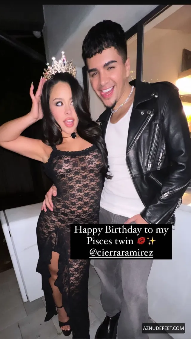 Cierra Ramirez in a black lace dress and platform sandals with her partner indoors.