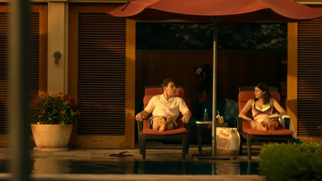 Alexandra Daddario sitting barefoot on a patio in a screen scene.