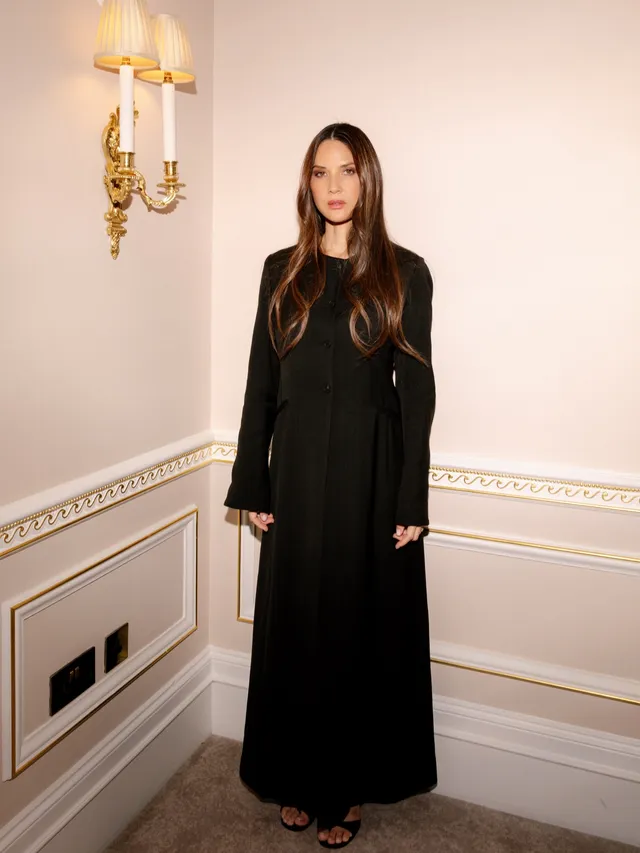 Olivia Munn posing in a black suit and strappy heels.