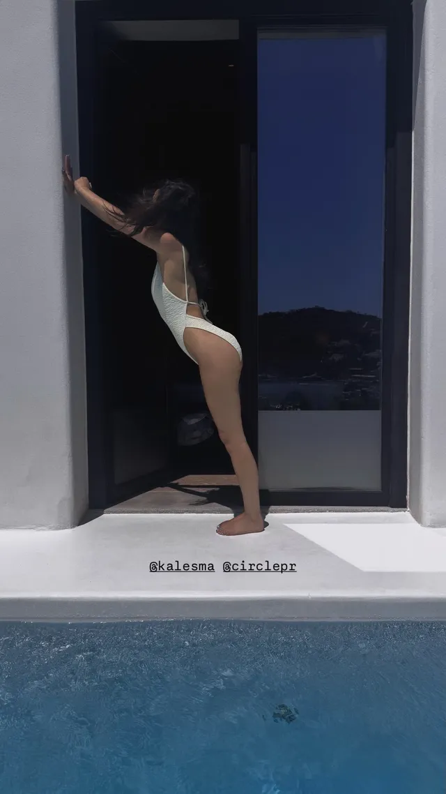 Rachel Zegler posing barefoot in a swimsuit by an open doorway.