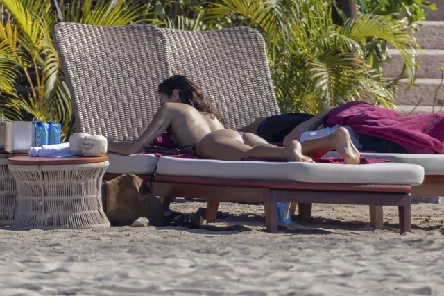 Dua Lipa: reclining barefoot on a sun lounger beside plants.
