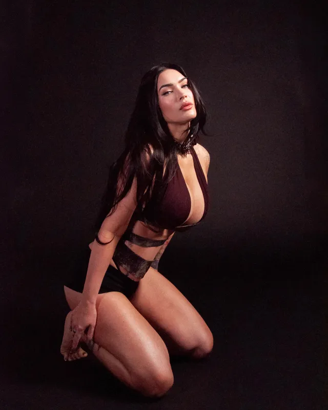 Megan Fox: kneeling barefoot in a dark studio portrait.