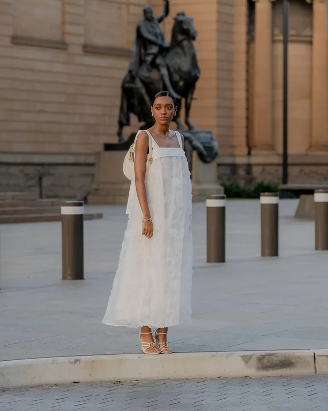 Sophie Wilde standing outdoors in a white dress and embellished heels.