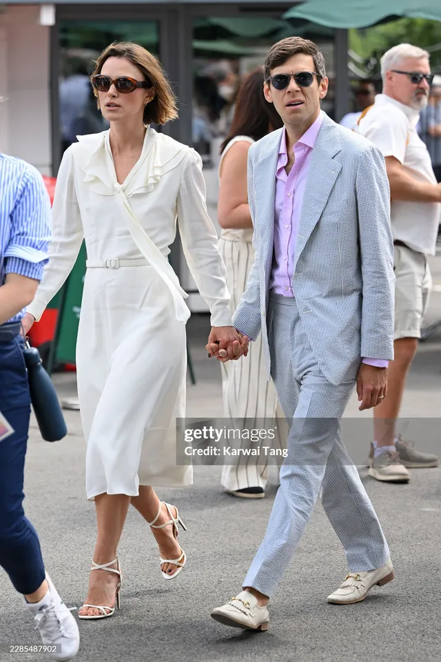 Keira Knightley walking outdoors in a white dress and strappy heels.