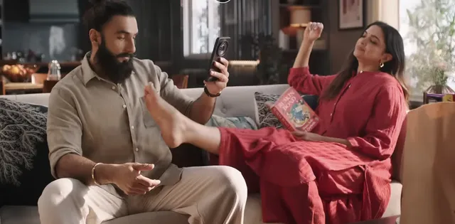 Deepika Padukone resting her bare foot beside a companion on a sofa.