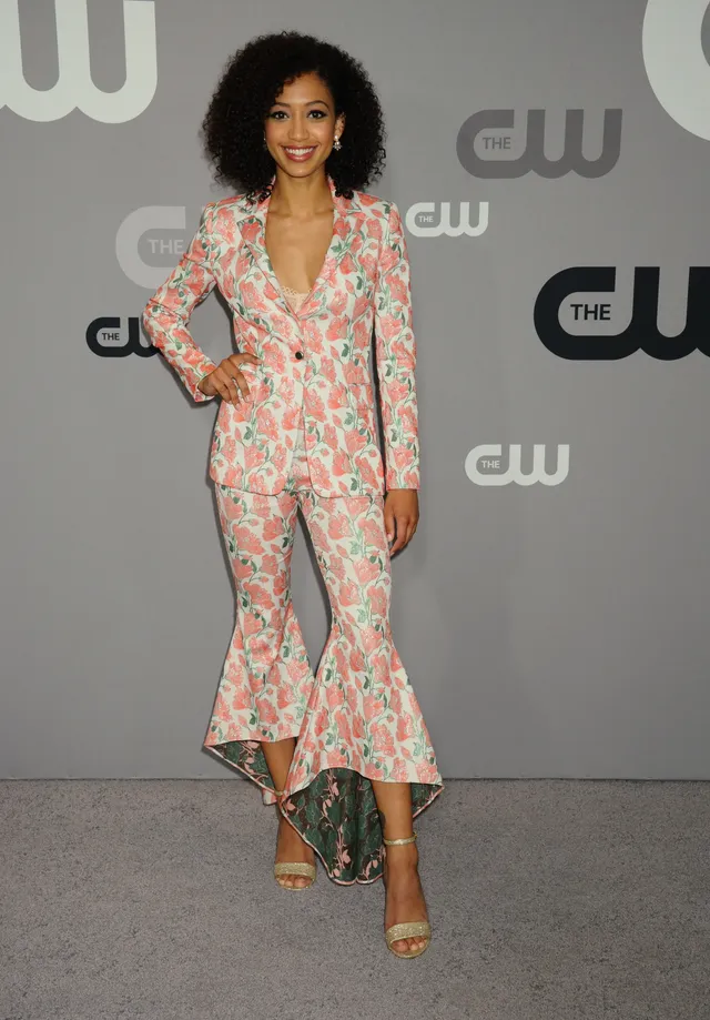 Samantha Logan wearing a floral trouser suit and gold heels at a CW event.