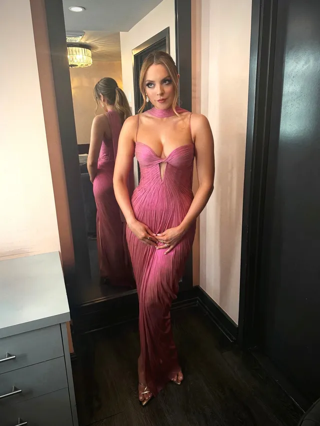 Elizabeth Gillies posing beside a mirror in a pink dress.