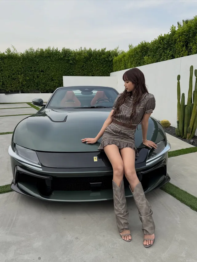 Lisa (Lalisa Manobal) sitting on a vehicle bonnet in tall open-toe heels and a patterned dress.