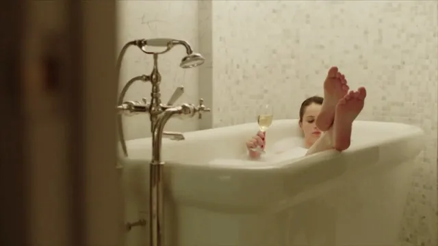 Felicity Jones raising a foot over the edge of a bathtub in a scene.