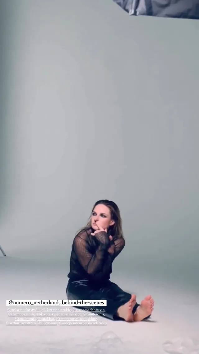 Rebecca Ferguson sitting on a studio floor with bare soles facing the camera.