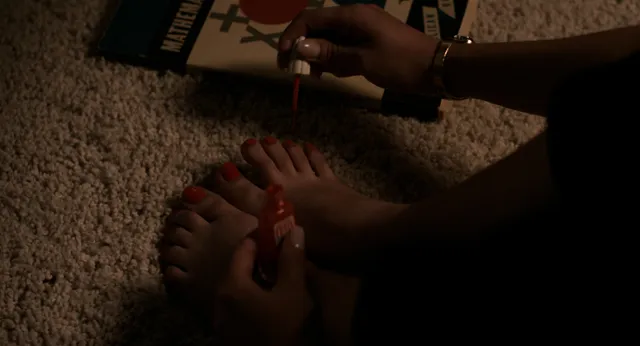 Cailee Spaeny painting her toenails while sitting on a carpet.