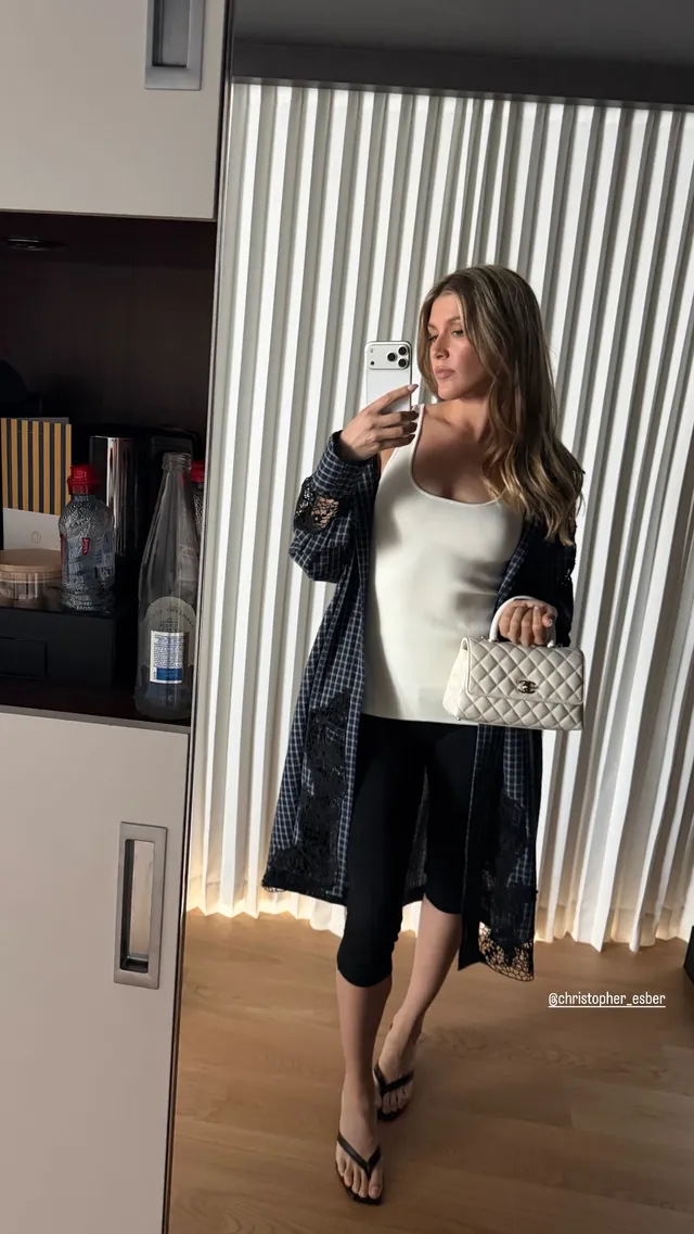 Eugenie Bouchard taking a mirror photograph in black flat sandals and a pale top with a dark skirt.