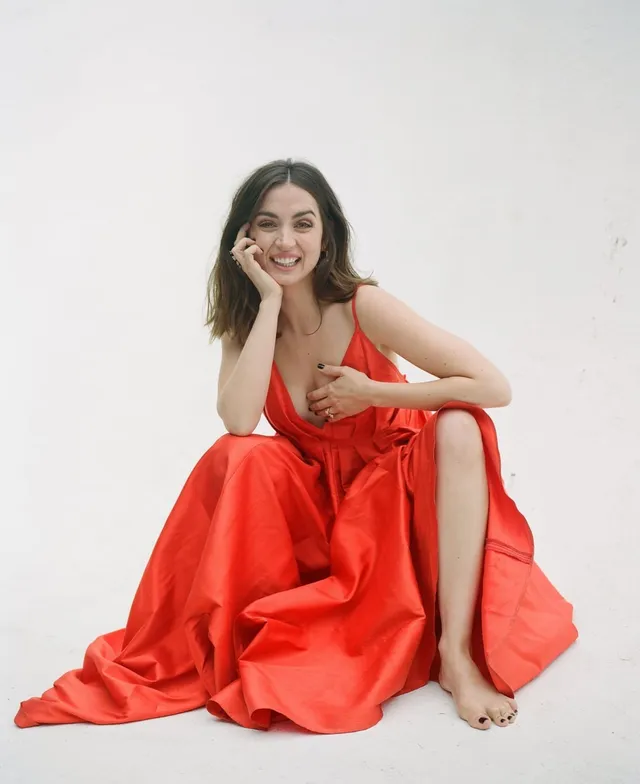 Ana de Armas: seated barefoot in a red dress in a studio portrait.