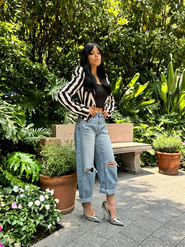 Jenna Ortega standing outdoors in jeans and silver heels.