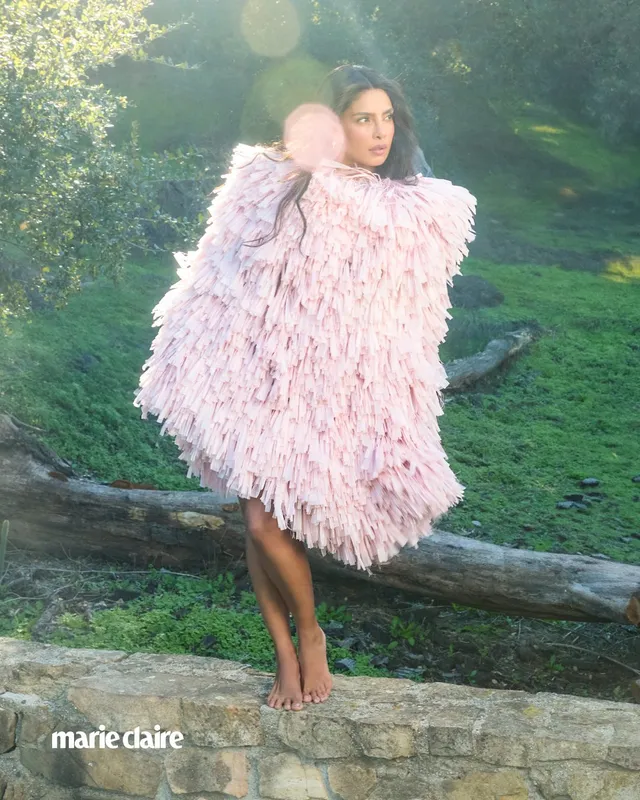 Priyanka Chopra Jonas wearing pale heeled sandals with a pink feathered outfit outdoors.