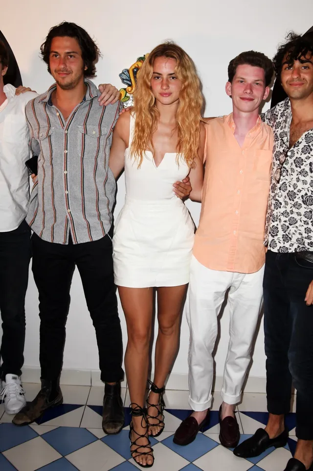 Grace Van Patten posing with a group in a white dress and lace-up heels.