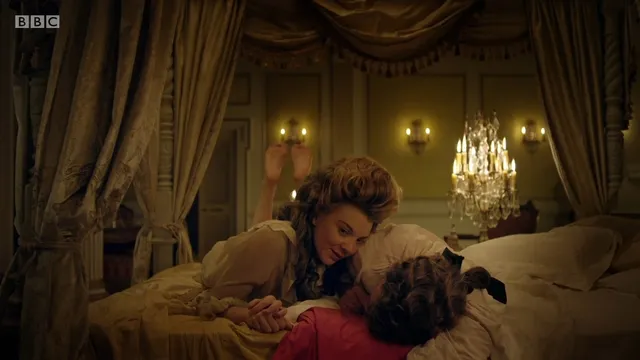 Natalie Dormer leaning over another performer in an ornate bedroom scene.