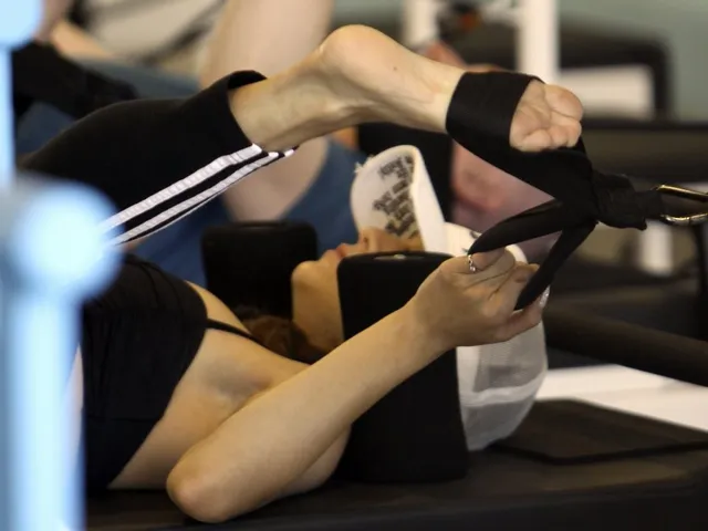 Vanessa Hudgens holding an exercise strap around a bare foot indoors.
