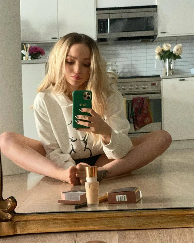 Dove Cameron sitting barefoot in front of a mirror.