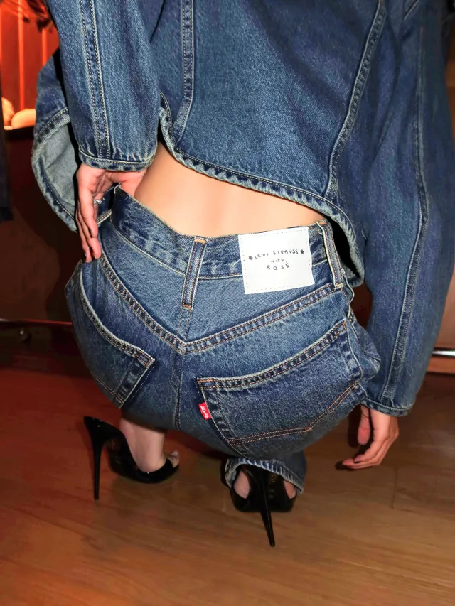 Rosé crouching in a denim outfit and black pointed-toe high heels, photographed from behind.