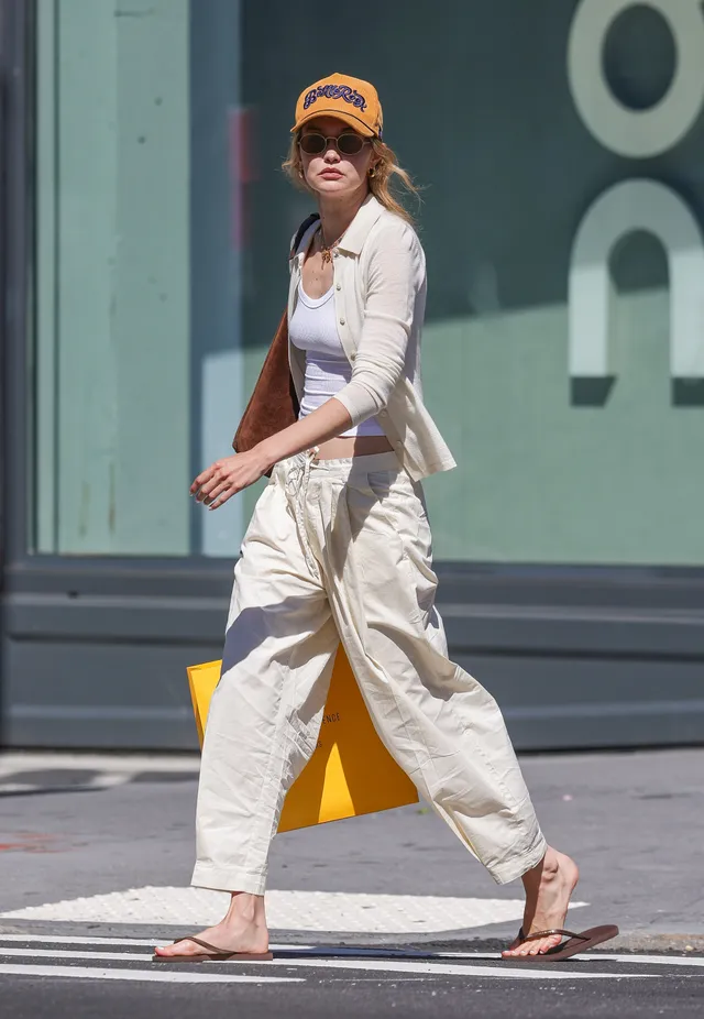 Gigi Hadid walking barefoot in pale trousers outdoors.