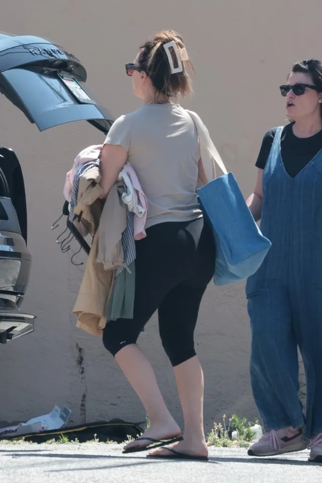 Kaley Cuoco standing beside a car in black leggings and flip-flops.