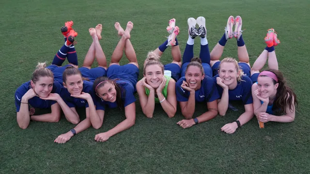Alex Morgan lying on grass with teammates during a group photograph.