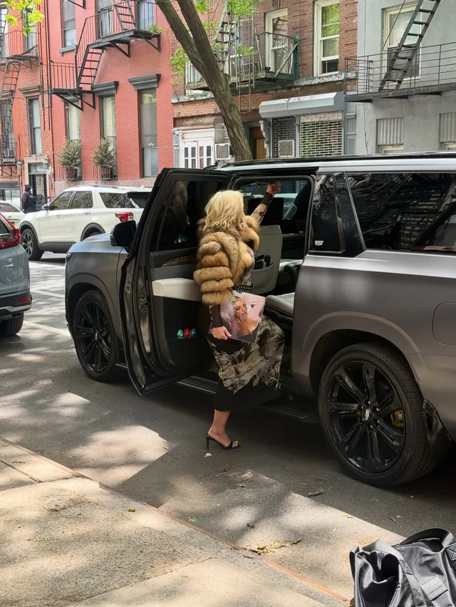 Bebe Rexha stepping beside a vehicle in a brown coat and heels.