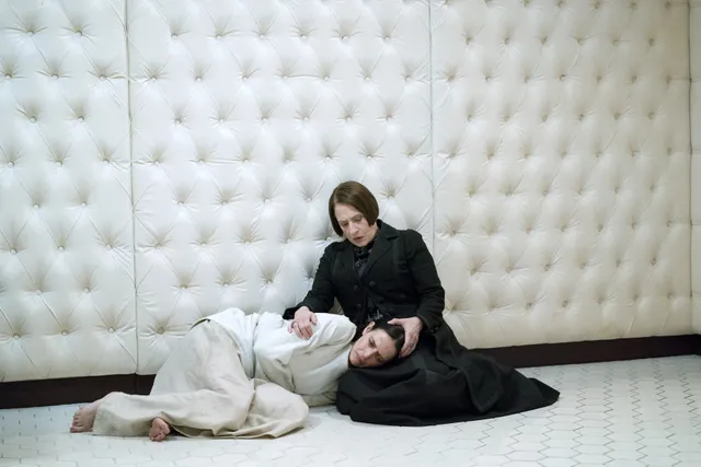 Eva Green sitting beside a reclining person in a padded room.