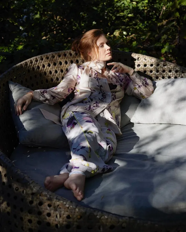 Amy Adams reclining on an outdoor sofa in a patterned outfit.