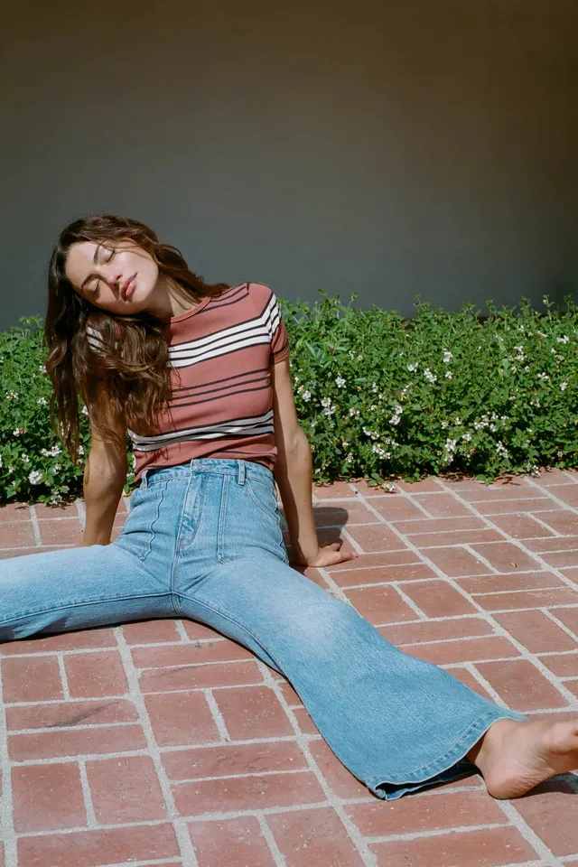 Phoebe Tonkin sitting on a tiled patio in jeans and a striped top.