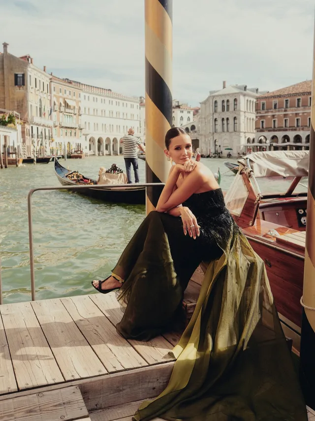 Nina Dobrev sitting beside a canal in a gown and heels.