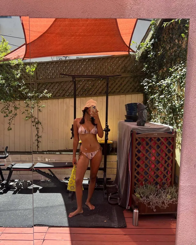 Greta Onieogou standing barefoot outdoors in a patterned bikini and sun hat.