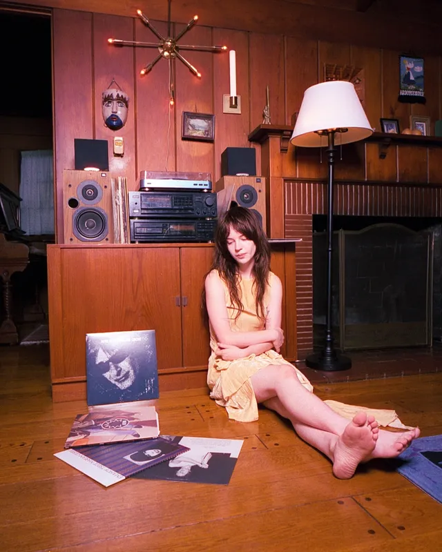Sophie Thatcher sitting barefoot on a wooden floor beside records.