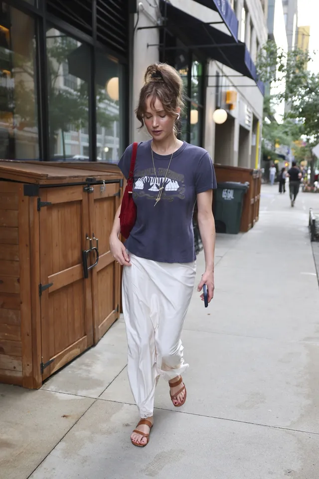 Jennifer Lawrence standing outdoors in a T-shirt and flat sandals.