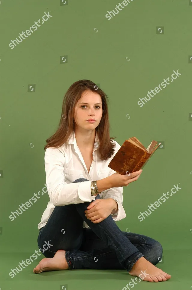 Felicity Jones sitting cross legged holding a book.