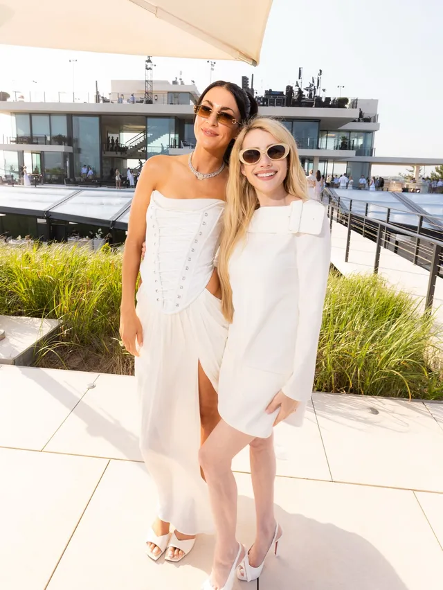 Emma Roberts posing beside a guest in a light dress and strappy heels.