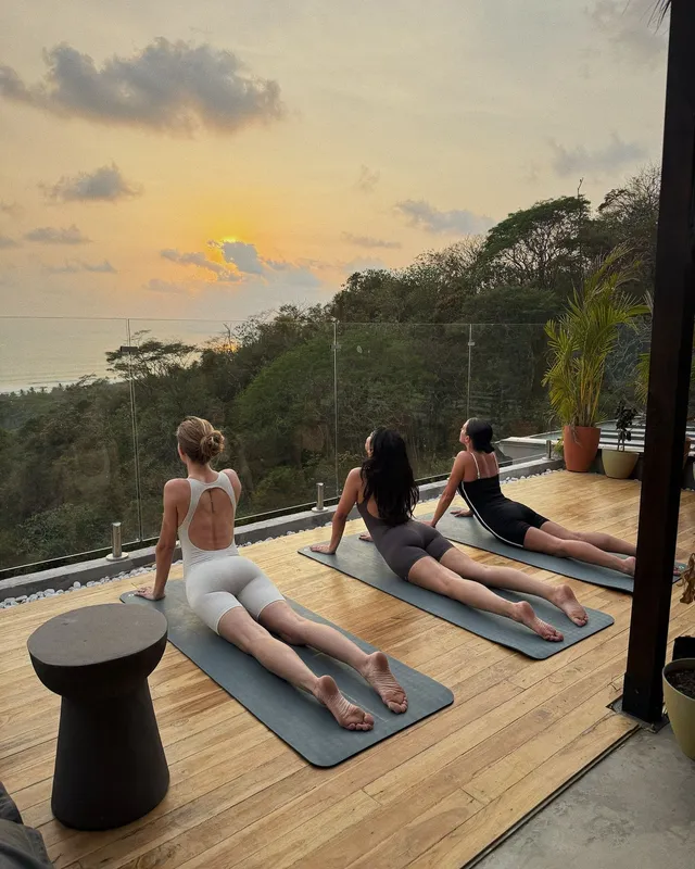 Josephine Skriver stretching barefoot on an outdoor exercise mat with companions at sunset.
