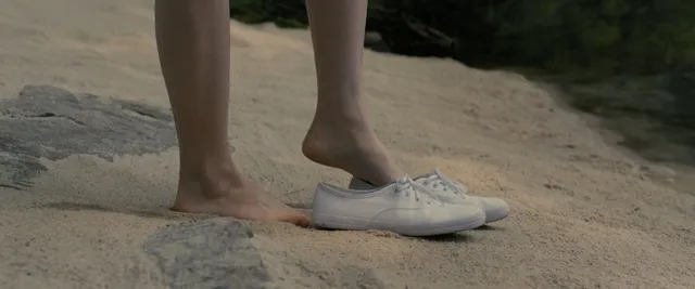 Sophie Thatcher standing barefoot beside a white trainer in a film scene.